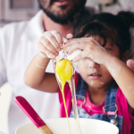 Father and daughter baking together. Daughter is cracking an egg into a bowl