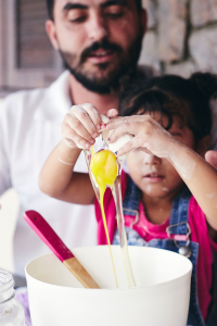 Father and daughter baking together. Daughter is cracking an egg into a bowl